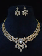 Gold-tone floral jewelry set featuring a statement necklace and matching stud earrings, embellished with clear rhinestones, displayed on a dark blue velvet neck stand against a black background.