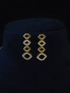 A pair of gold geometric drop earrings with clear pavé-set stones, displayed on a black velvet jewelry bust.