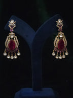 Pair of traditional chandelier earrings with wine-red center stones and clear dangling accents displayed on dark velvet.