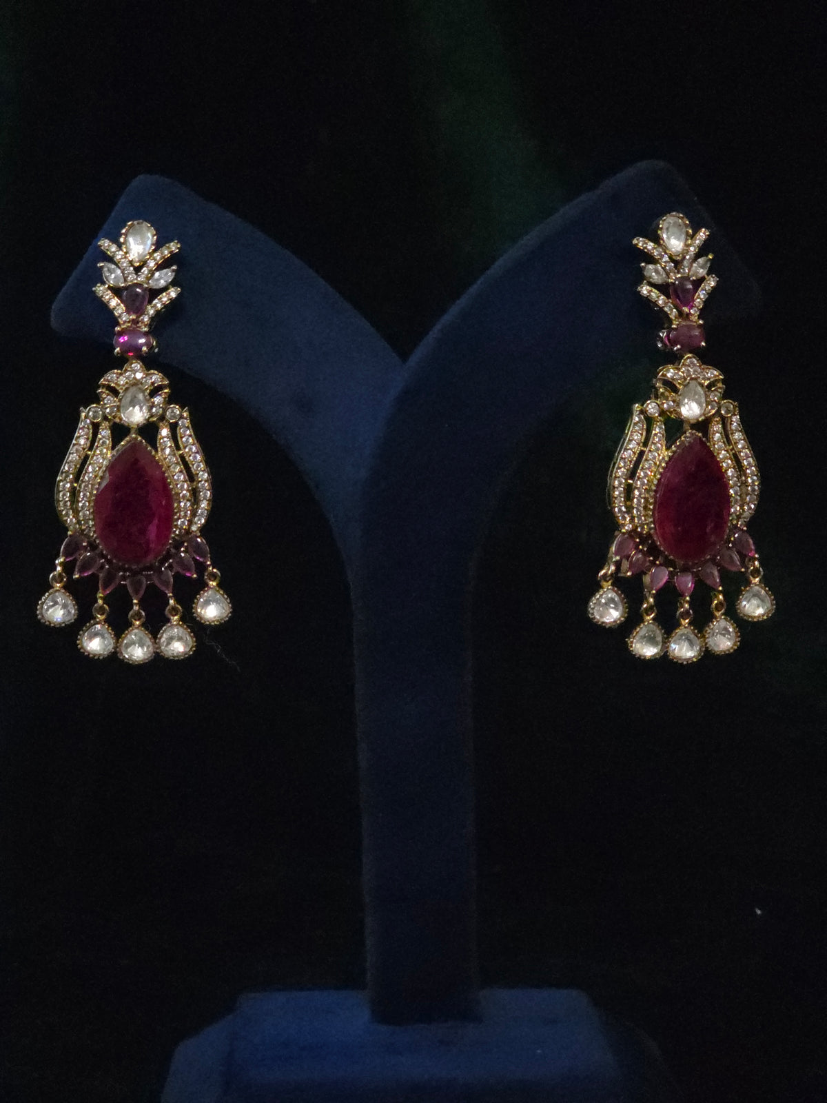 Pair of traditional chandelier earrings with wine-red center stones and clear dangling accents displayed on dark velvet.