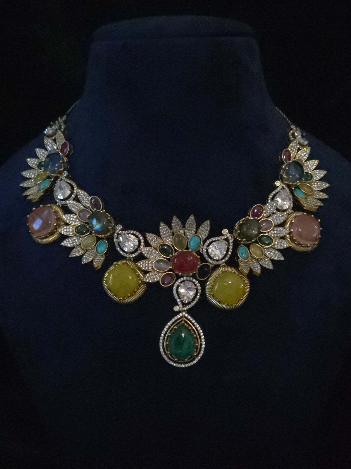 Multicolor gemstone leaf necklace and matching drop earrings displayed together on a jewelry stand