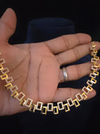 A gold and white stone chain necklace draped over a person's hand,  set against a dark background.