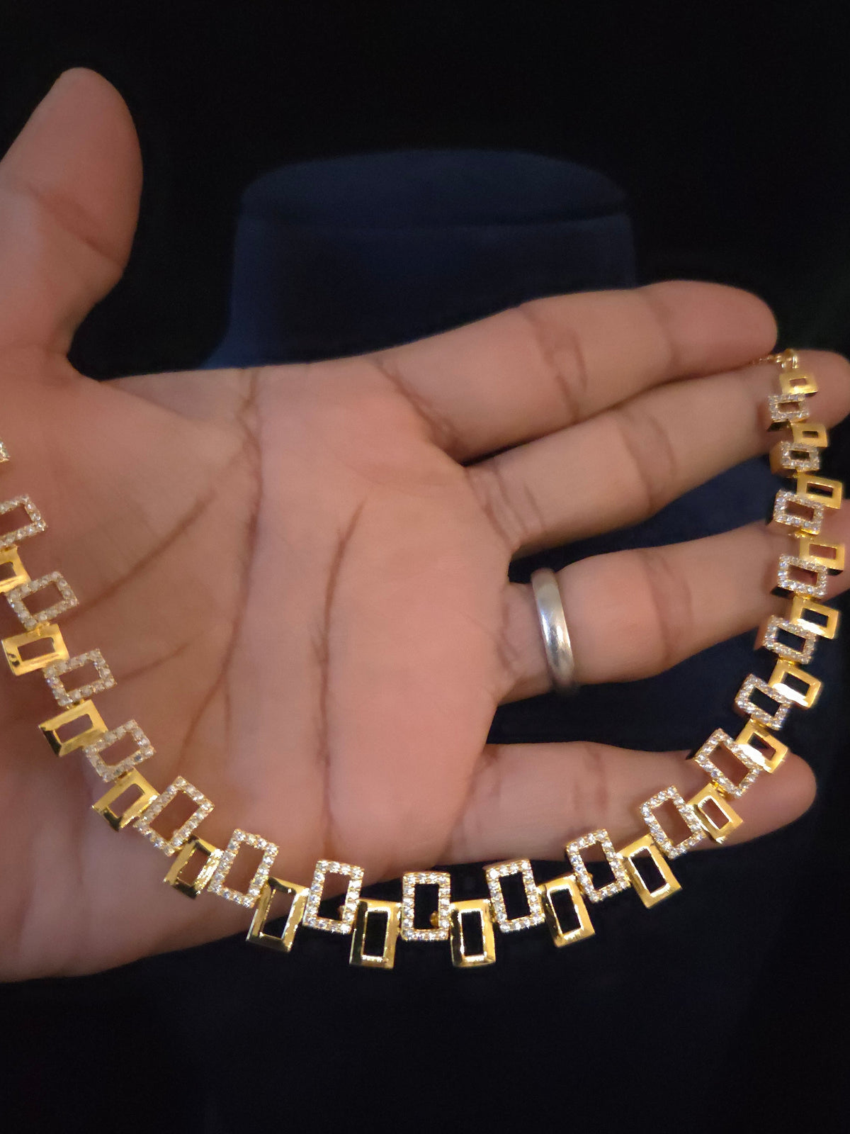 A gold and white stone chain necklace draped over a person's hand,  set against a dark background.