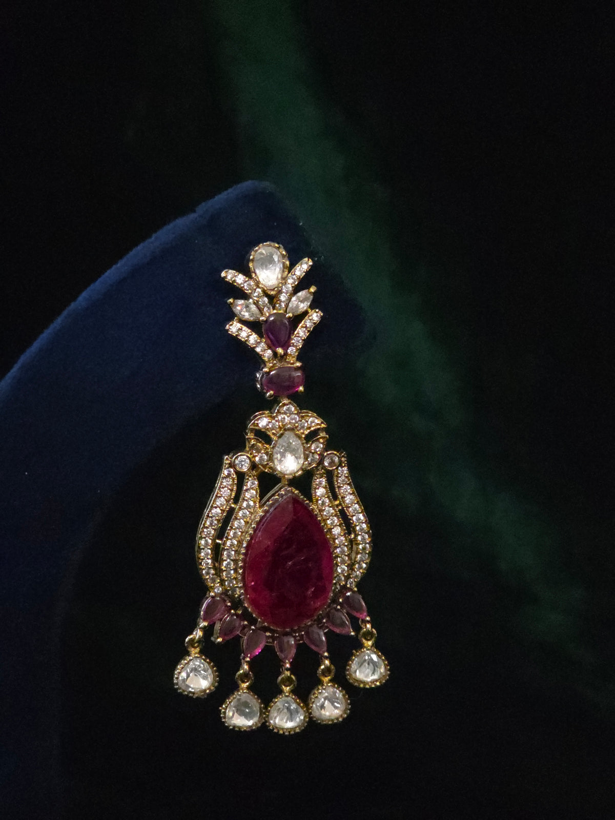 Close-up of a matching chandelier earring with wine-red stones, clear accents, and teardrop dangles
