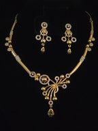 Gold-toned traditional Indian jewelry set featuring a necklace and matching earrings with intricate beadwork, floral motifs, and clear stone accents, displayed on a black background.