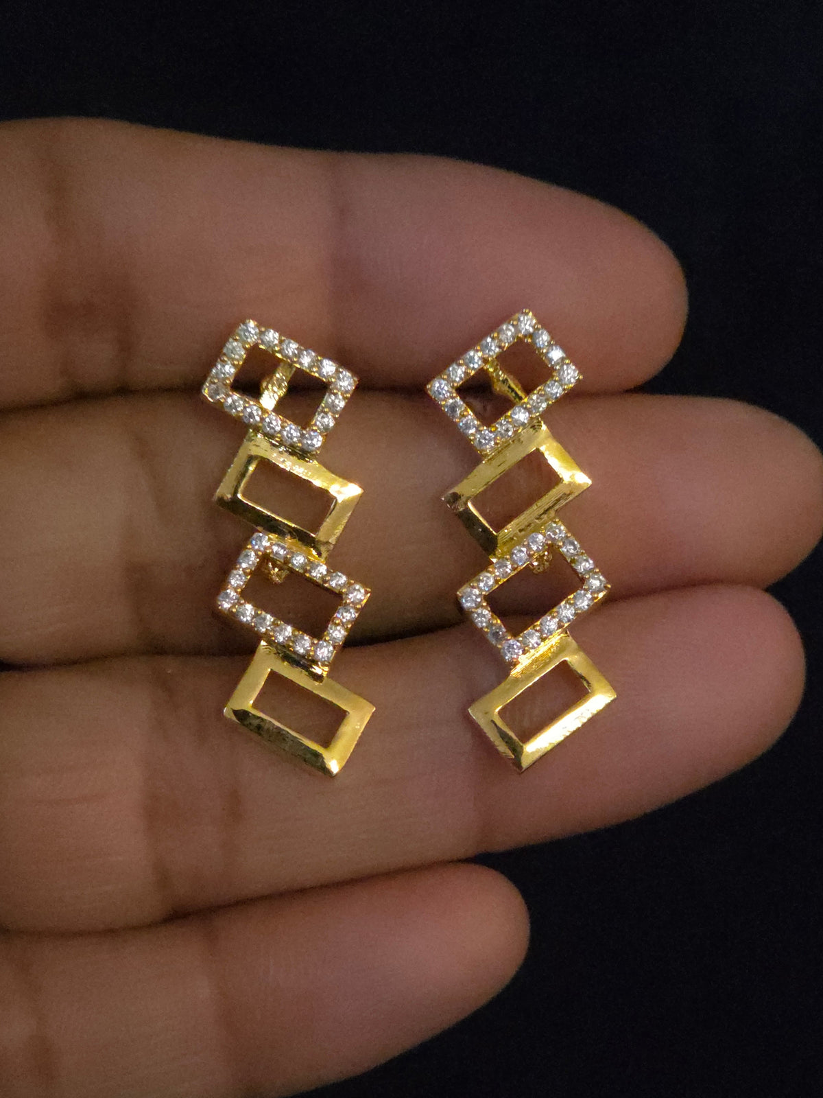 A gold and silver geometric drop earrings, displayed on a human hand