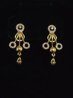 A pair of gold-toned traditional Indian jhumka earrings embellished with clear pavé stones in circular motifs and dangling bell charms, displayed on a black background.