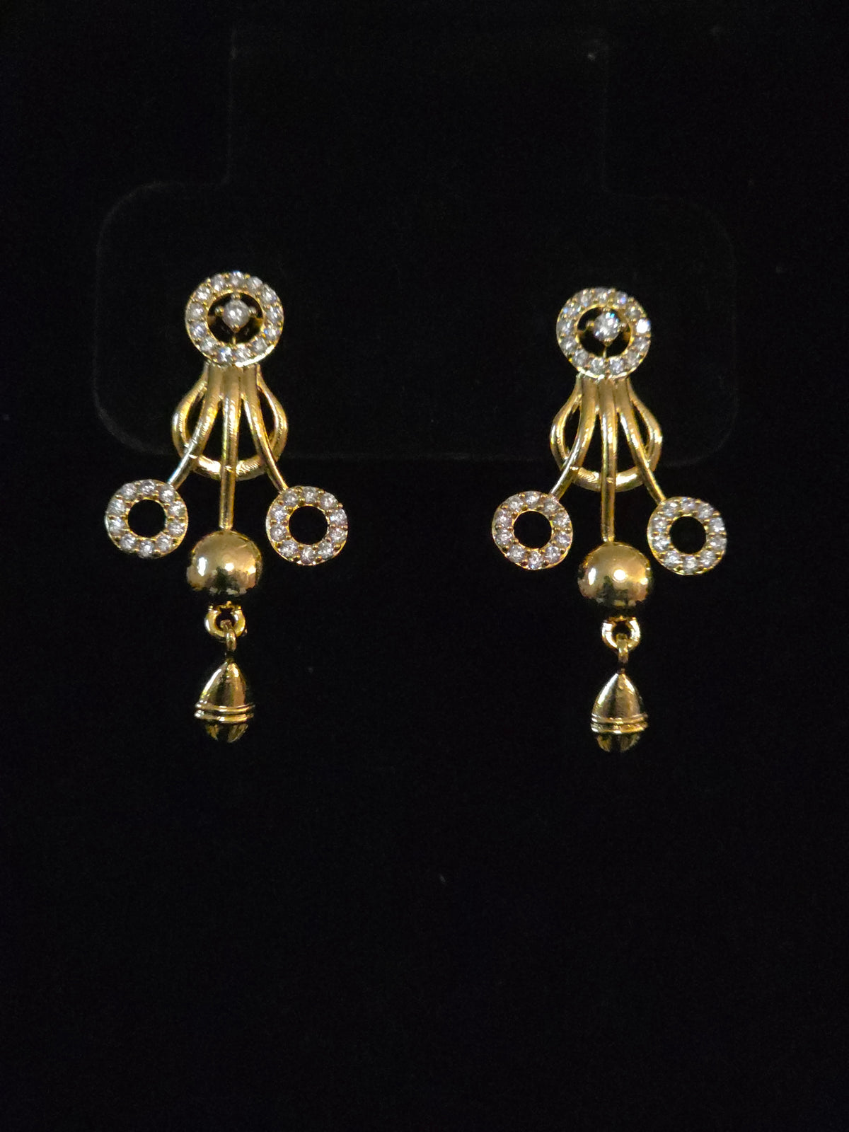 A pair of gold-toned traditional Indian jhumka earrings embellished with clear pavé stones in circular motifs and dangling bell charms, displayed on a black background.